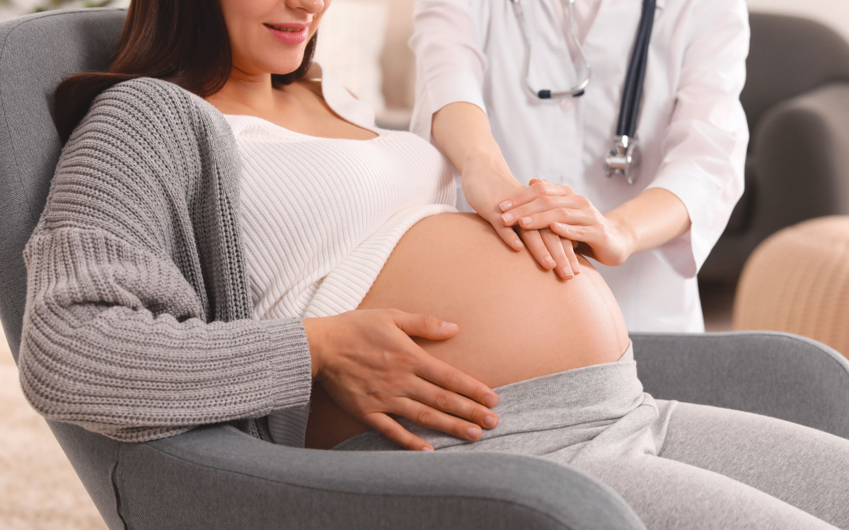 Pregnant person sitting with doctor examining their stomach 